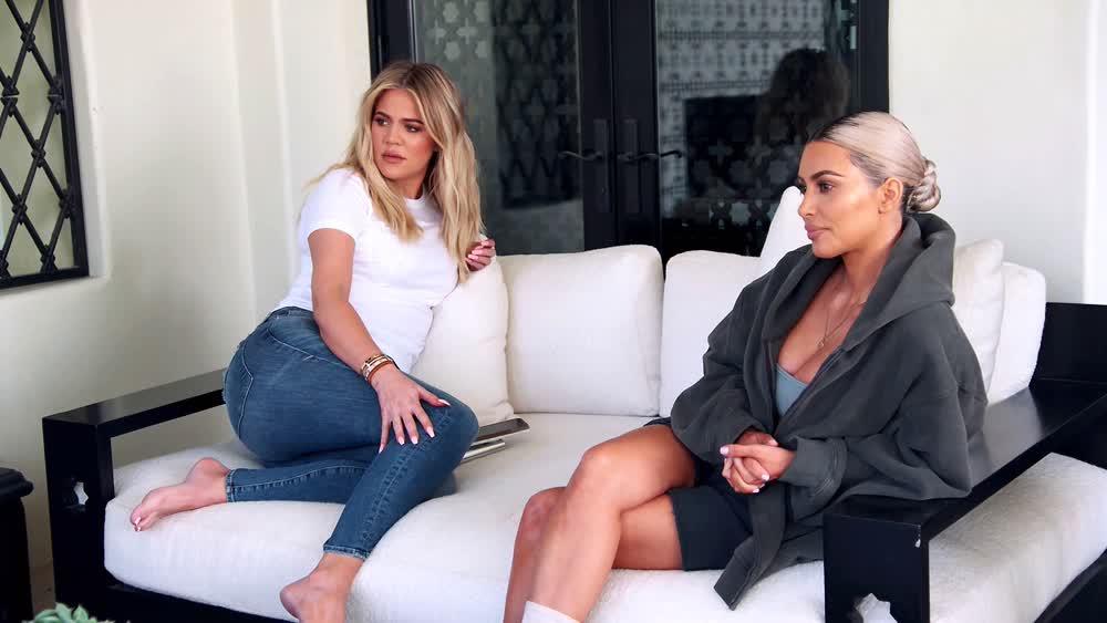 Khloe Kardashian and Kim Kardashian sitting on the couch, waiting for Kourtney